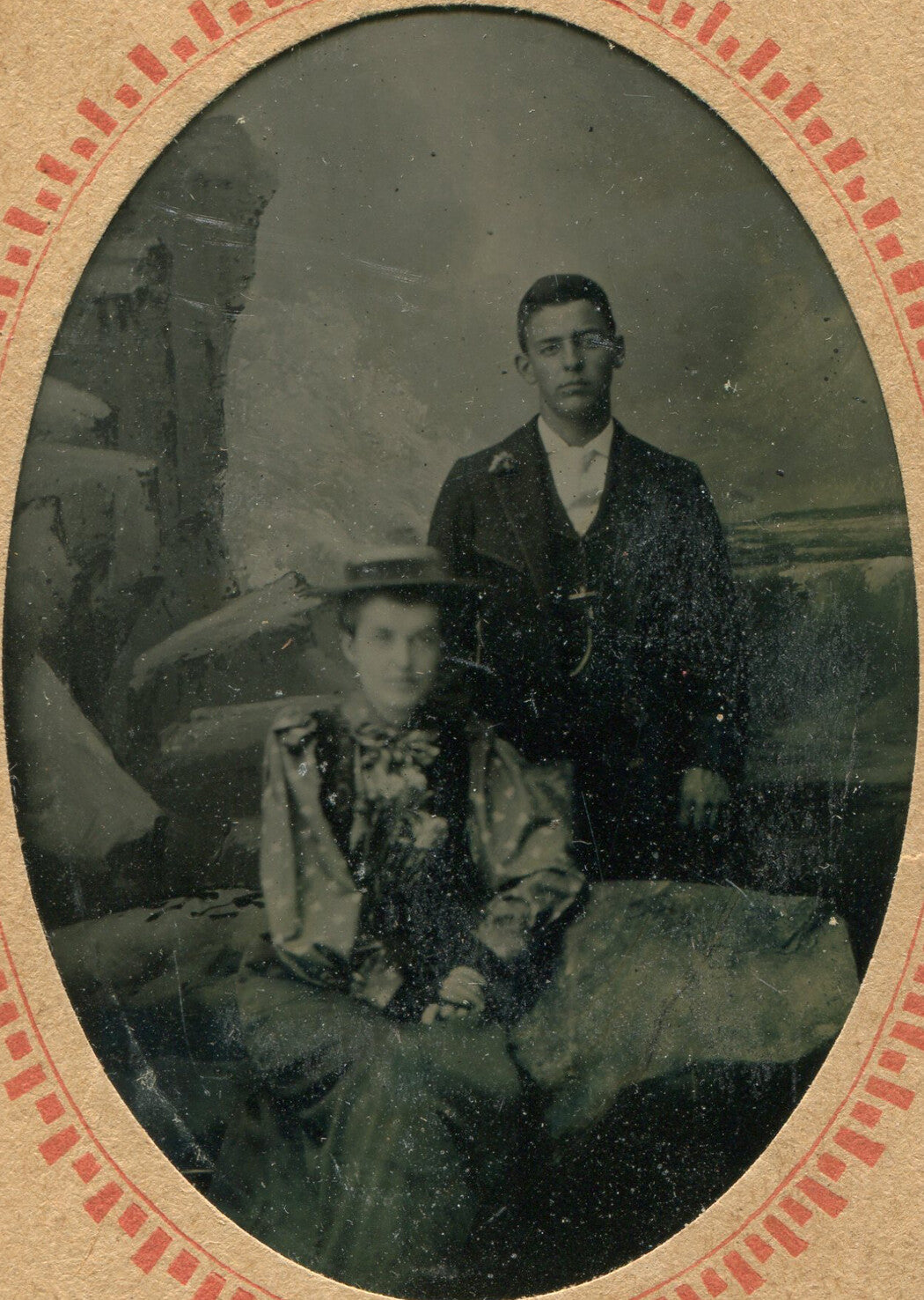GLUM MAN, WOMAN IN HAT. TINTYPE, PAINTED BACKGROUND, PERIOD PAPER MAT.