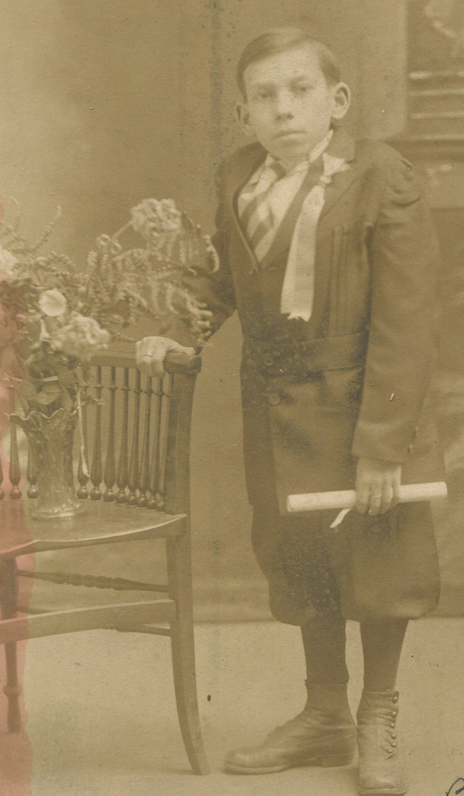 BOY WITH ODD PHYSICAL PROPORTIONS, RIBBON PINNED TO SUIT, HOLDING DIPLOMA.