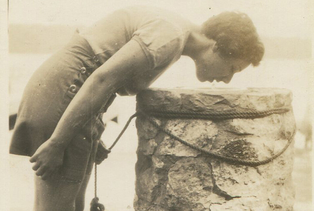 YOUNG WOMAN IN SHORT SKIRT BENT OVER AT DRINKING FOUNTAIN. 1940s.
