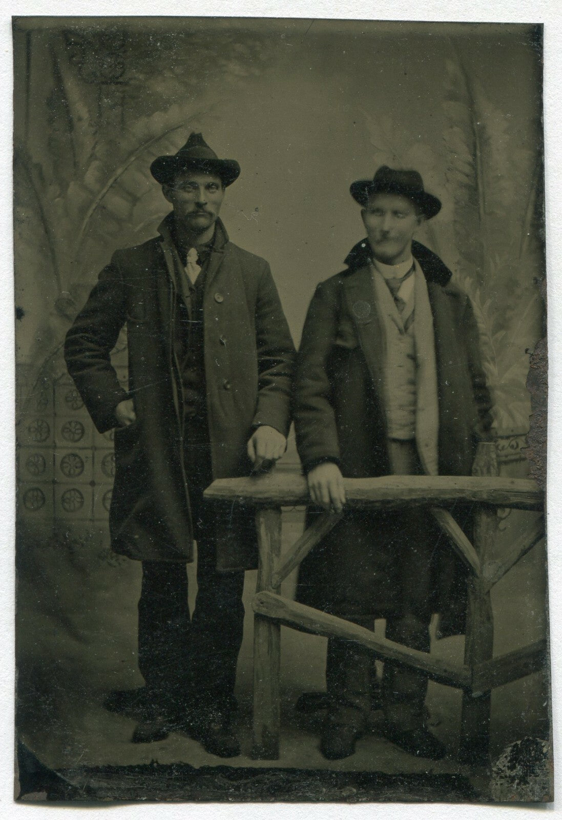 TWO MEN IN SUITS W/HATS, OVERCOATS. TINTYPE, PAINTED BACKGROUND.