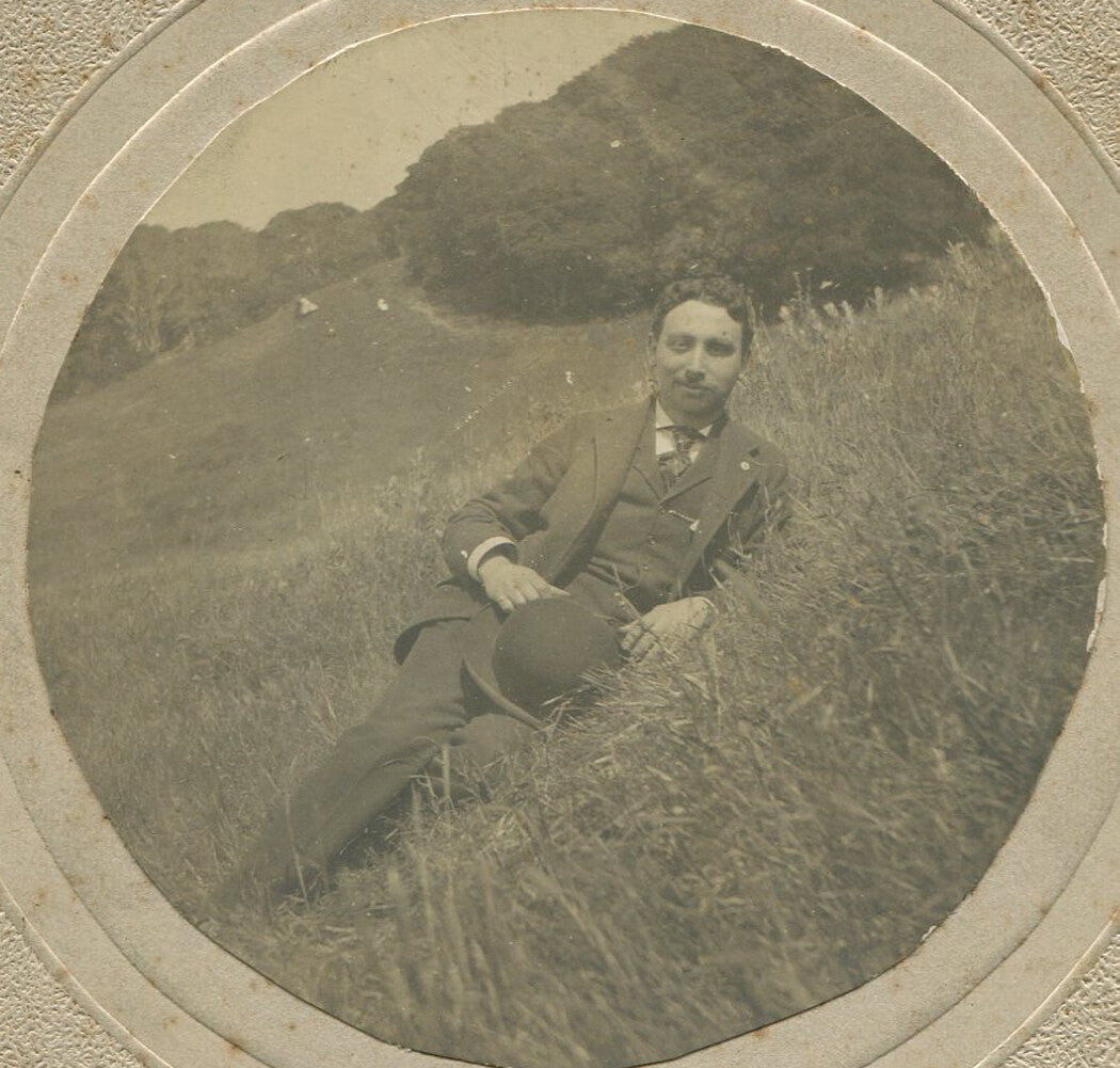 MAN HOLDING BOWLER HAT, RECLINING IN FIELD. EARLY AMATEUR PHOTO. CIRCA 1900.