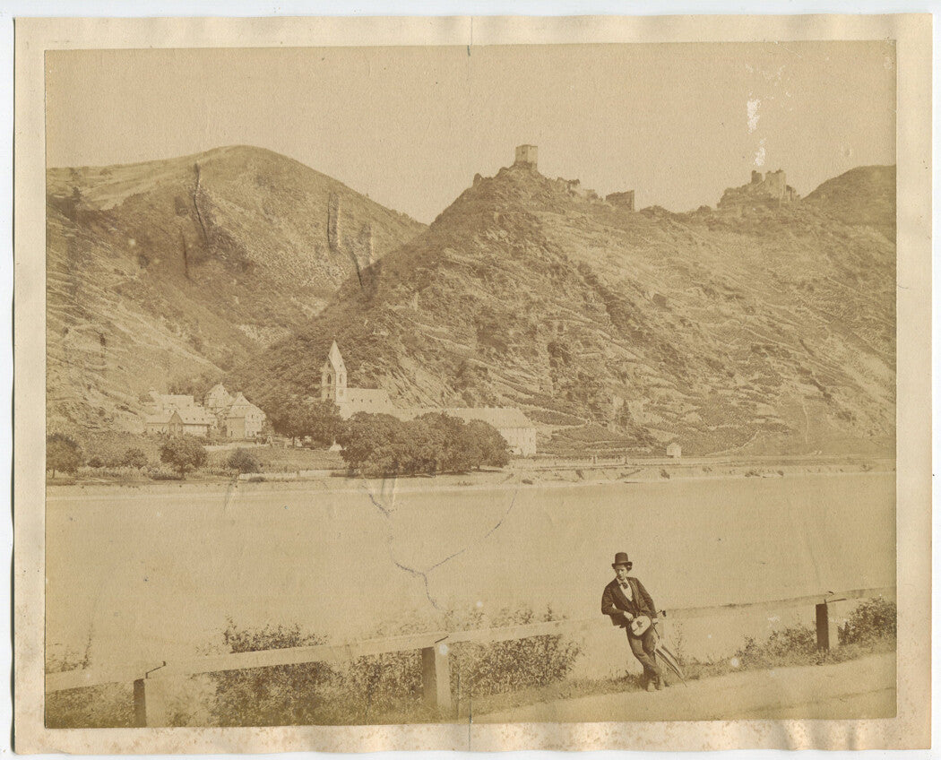 MAN IN TOP HAT W/ BAG, UMBRELLA. EUROPEAN VILLAGE IN BACKGROUND. ALBUMEN 1890.