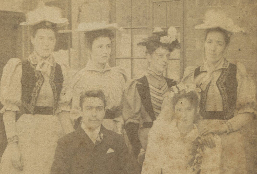 MAN, SEATED, WITHSTANDING ONSLAUGHT OF WOMEN IN HATS. CABINET CARD.