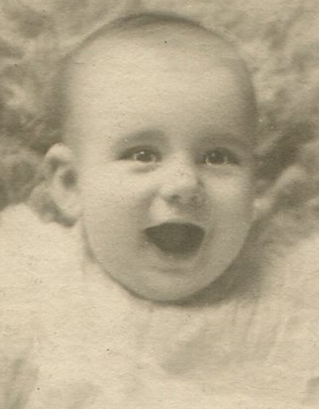 LAUGHING BABY, POSED ON CHAIR WITH FUR BLANKET.