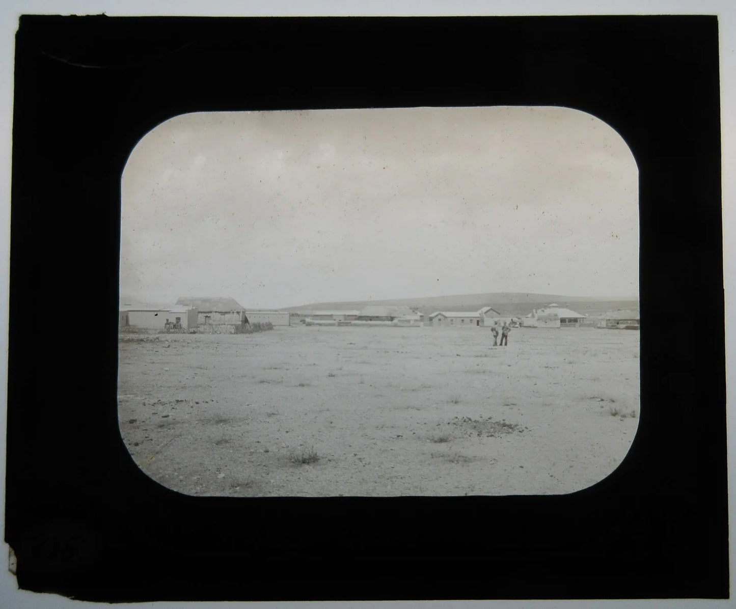TWO MEN IN FIELD, BUILDINGS/THATCHED ROOFS. LANTERN SLIDE.