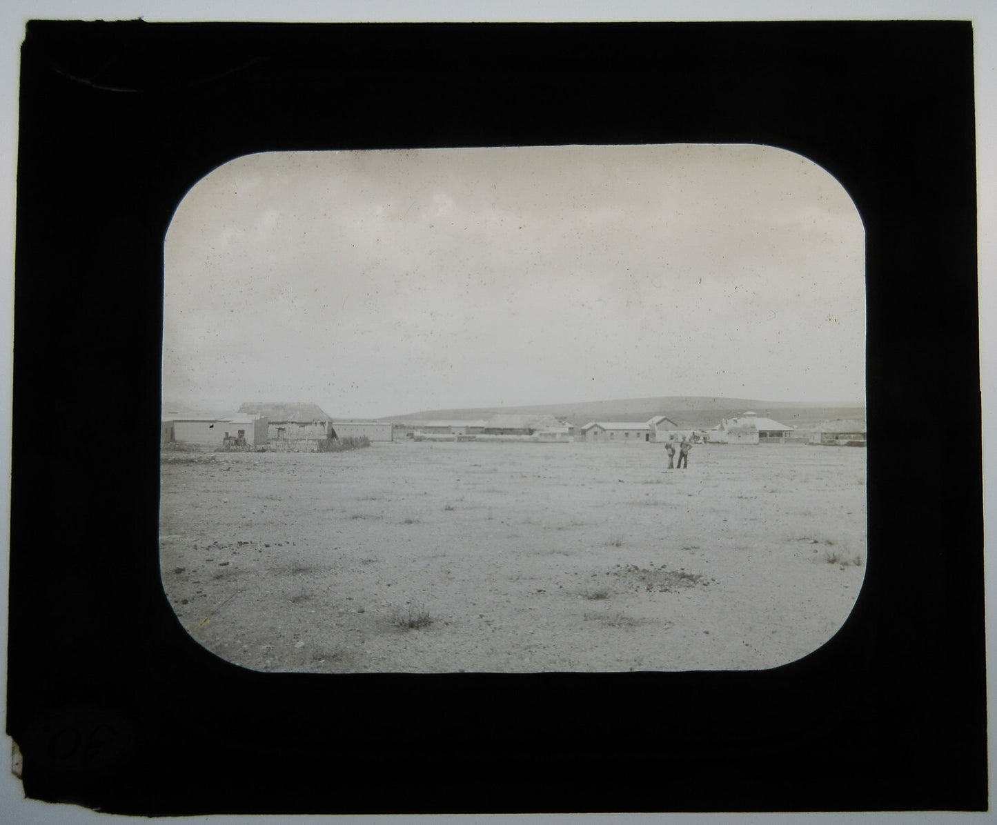 TWO MEN IN FIELD, BUILDINGS/THATCHED ROOFS. LANTERN SLIDE.