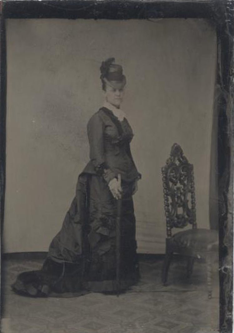 TINTYPE, WOMAN STANDING WITH CHAIR WEARING A FANCY DRESS AND FEATHERED HAT.