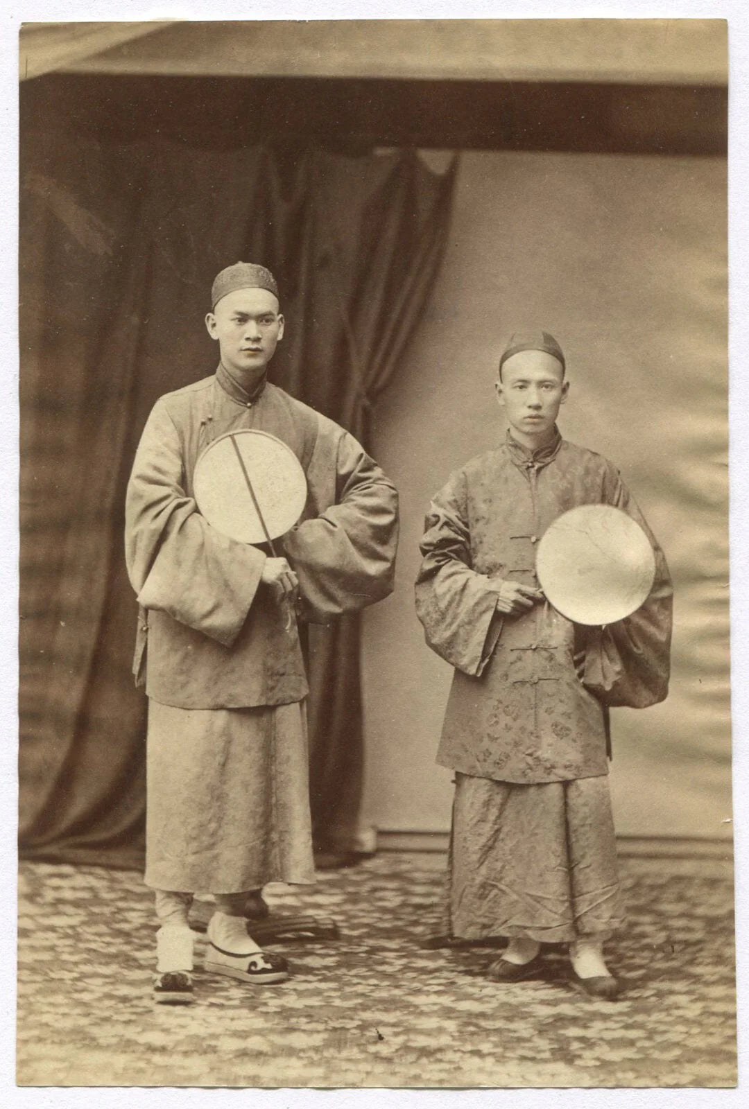TWO CHINESE MEN, TRADITIONAL ATTIRE, HOLDING DRUMS. 1880s. TINTED ALBUMEN.
