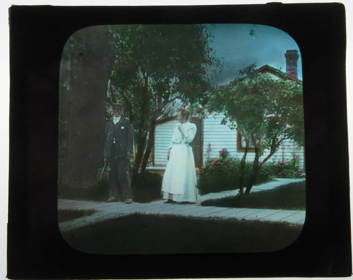 COUPLE POSED IN FRONT OF MODEST HOME. LOVELY HAND COLORED PHOTO ON GLASS.