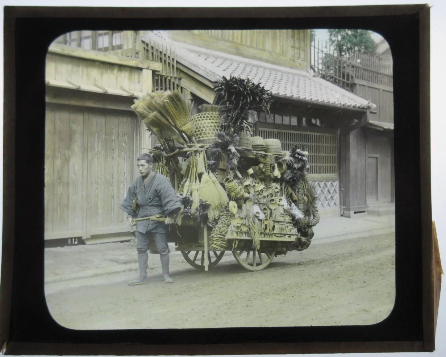 MAN PULLING VENDING CART, HOUSEWARES, JAPAN. HAND COLORED PHOTO ON GLASS.