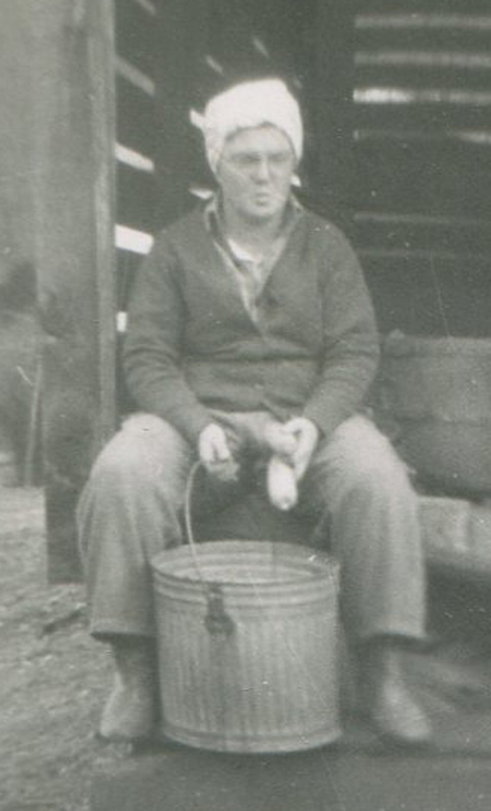 WOMAN SHELLING CORN INTO METAL BUCKET. 1950 SILVER PRINT, 4.5 X 3.25 INCHES.