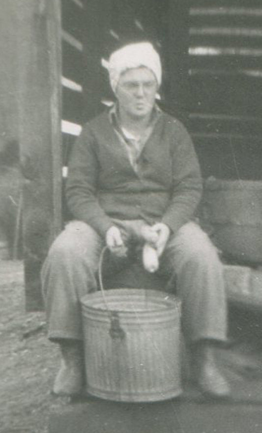 WOMAN SHELLING CORN INTO METAL BUCKET. 1950 SILVER PRINT, 4.5 X 3.25 INCHES.