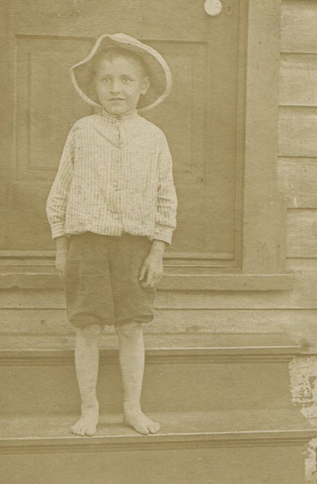 BOY IN FLOPPY HAT AND SHORTS STANDING ON STEPS. PITTSBURGH, PA. CIRCA 1930.