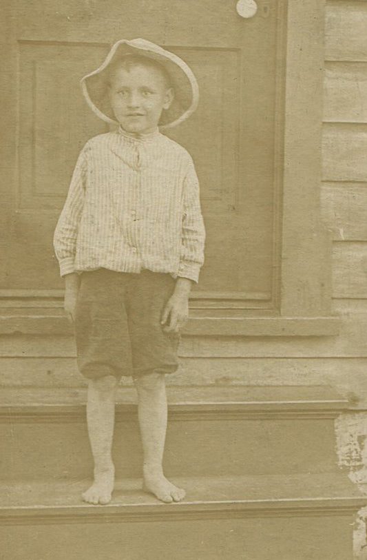 BOY IN FLOPPY HAT AND SHORTS STANDING ON STEPS. PITTSBURGH, PA. CIRCA 1930.