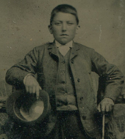 BOY POSED HOLDING HAT AND CANE, RUSTIC SETTING. TINTYPE.