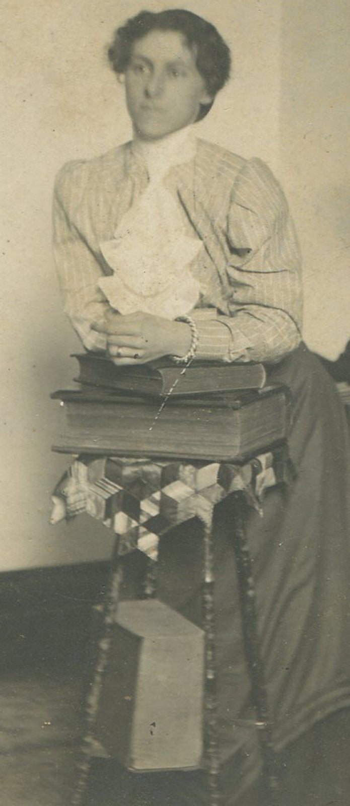 WOMAN LEANING ON STACK OF BOOKS, INTERIOR. SILVER PRINT, CIRCA 1900.