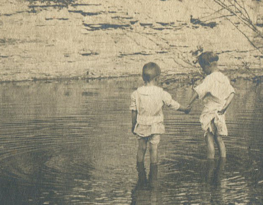 YOUNG SIBLINGS WADE IN SHALLOW WATER. BEAUTIFULLY COMPOSED.TONED SILVER PRINT.