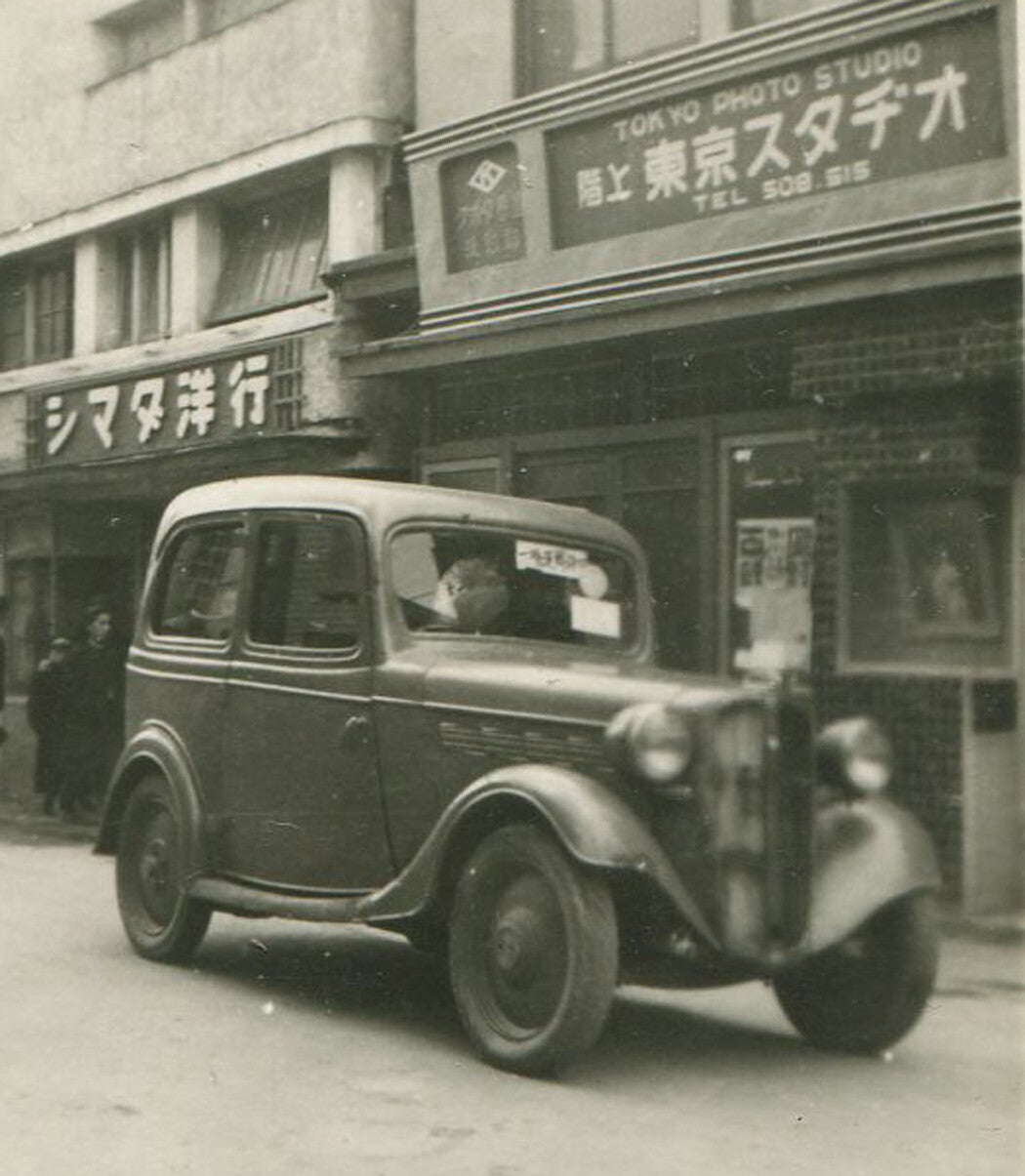 EARLY MODEL JAPANESE CAR, 1930-40s. TOKYO PHOTO STUDIO IN BACKGROUND. B W.