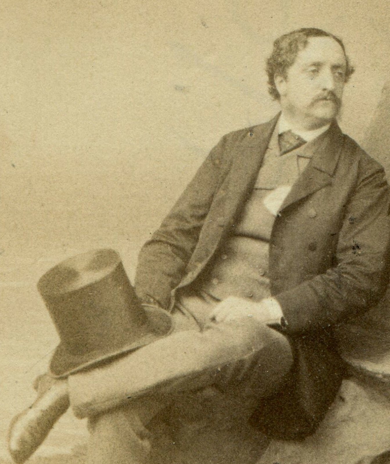 MAN IN RELAXED SEATED POSE ON ROCKS, HOLDING TOPHAT. STUDIO SETTING. CDV. LONDON