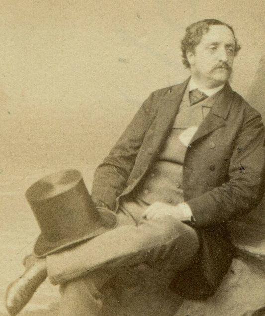 MAN IN RELAXED SEATED POSE ON ROCKS, HOLDING TOPHAT. STUDIO SETTING. CDV. LONDON