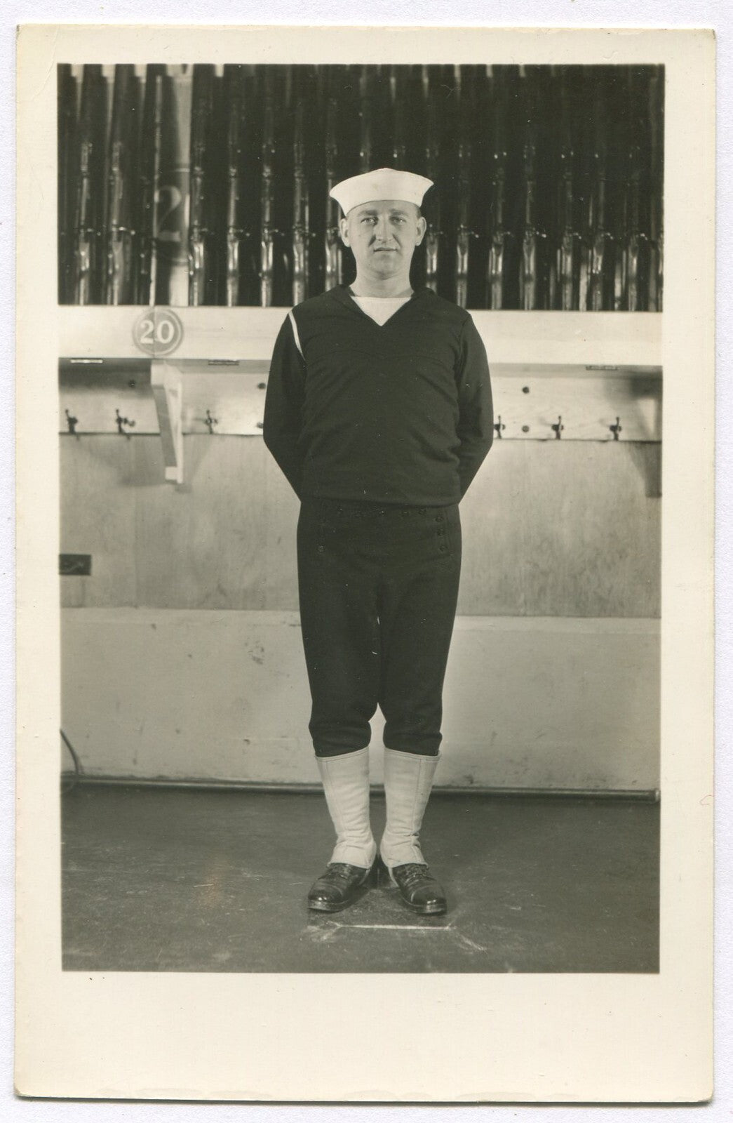 Vintage black-and-white photograph of U.S. sailor in front of gun rack, 5.5x3.5 in, original photo wall decor