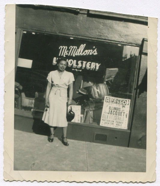 AFRICAN AMERICAN WOMAN POSED IN FRONT OF UPHOLSTERY SHOP. B&W SNAPSHOT.