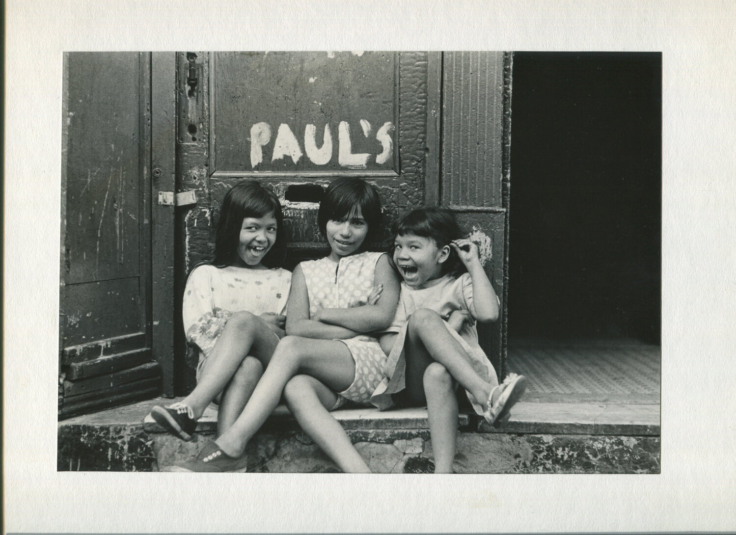 THREE LITTLE GIRLS MUG FOR THE CAMERA OUTSIDE PAUL'S MAILSLOT. B&W PHOTO, 1970s.