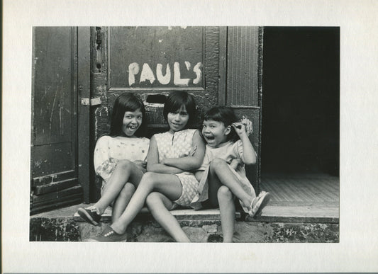 THREE LITTLE GIRLS MUG FOR THE CAMERA OUTSIDE PAUL'S MAILSLOT. B&W PHOTO, 1970s.