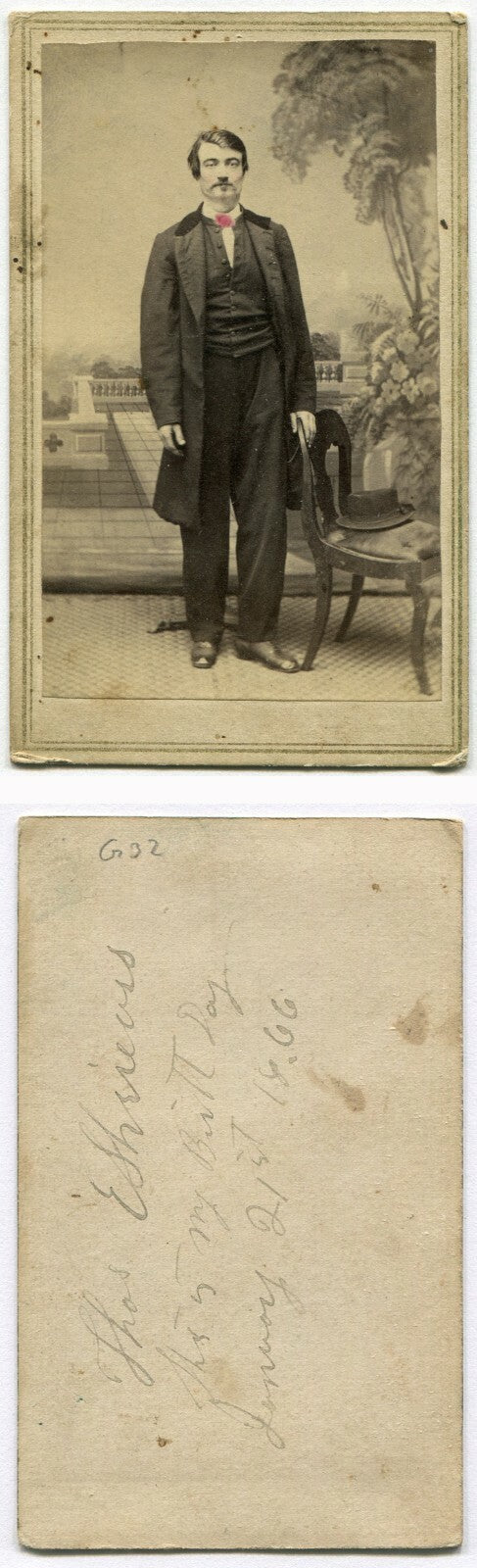MAN W/HAT AT POSING STAND, PAINTED BACKGROUND. TINTED CDV. DATED 1866.