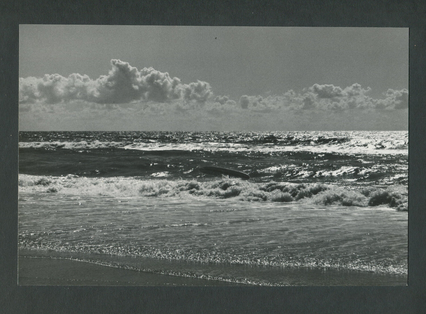 EMPTY SURFBOARD COMING TO SHORE. OCEAN BEACH SCENE. B&W PHOTO. 1970s.