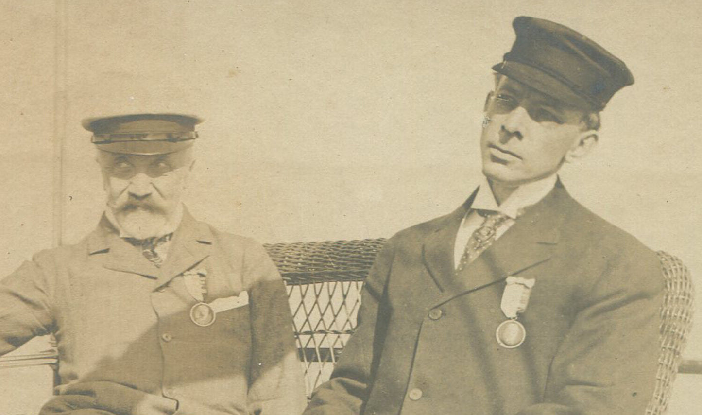 TWO MEN W/RIBBON/METAL, POSED SEATED ON SHIP DECK. 5X7 TONED B&W. 1900-20.