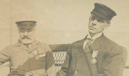 TWO MEN W/RIBBON/METAL, POSED SEATED ON SHIP DECK. 5X7 TONED B&W. 1900-20.