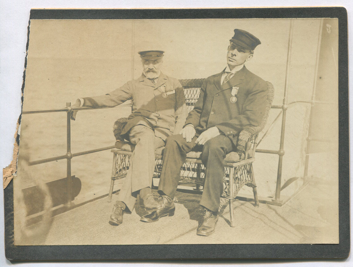 TWO MEN W/RIBBON/METAL, POSED SEATED ON SHIP DECK. 5X7 TONED B&W. 1900-20.