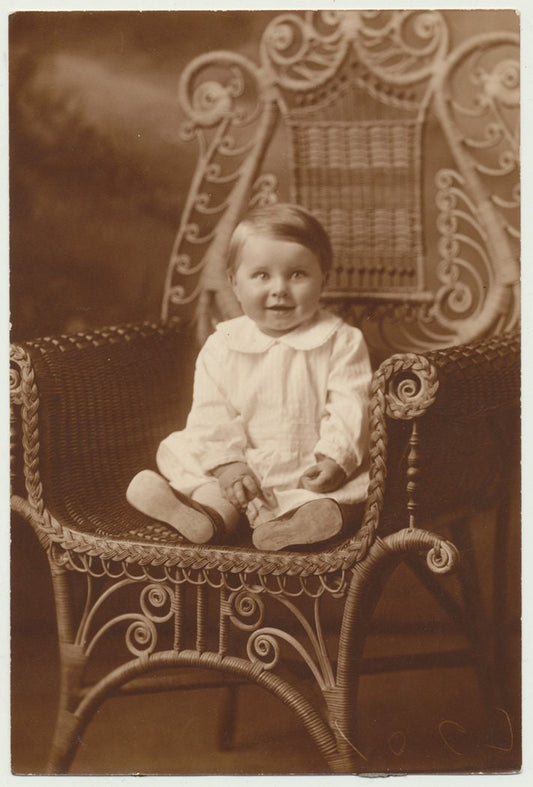 Cute but Scary Baby Smiling on an Ornate Chair. Sepia Toned Print.