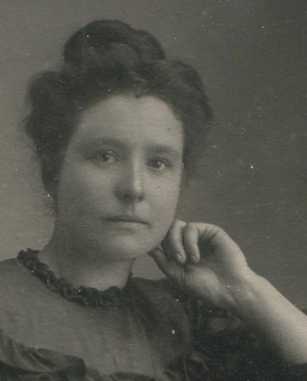 Vintage toned portrait photograph of a woman with hand at chin in a ruffle