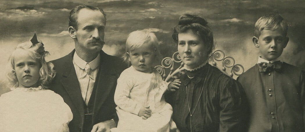 Vintage family photo: parents with three children, painted ocean backdrop,