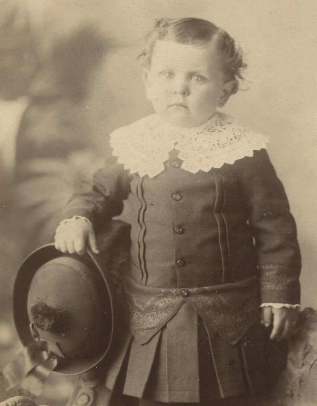 Vintage cabinet card portrait: chubby toddler with hat and unhappy expression,