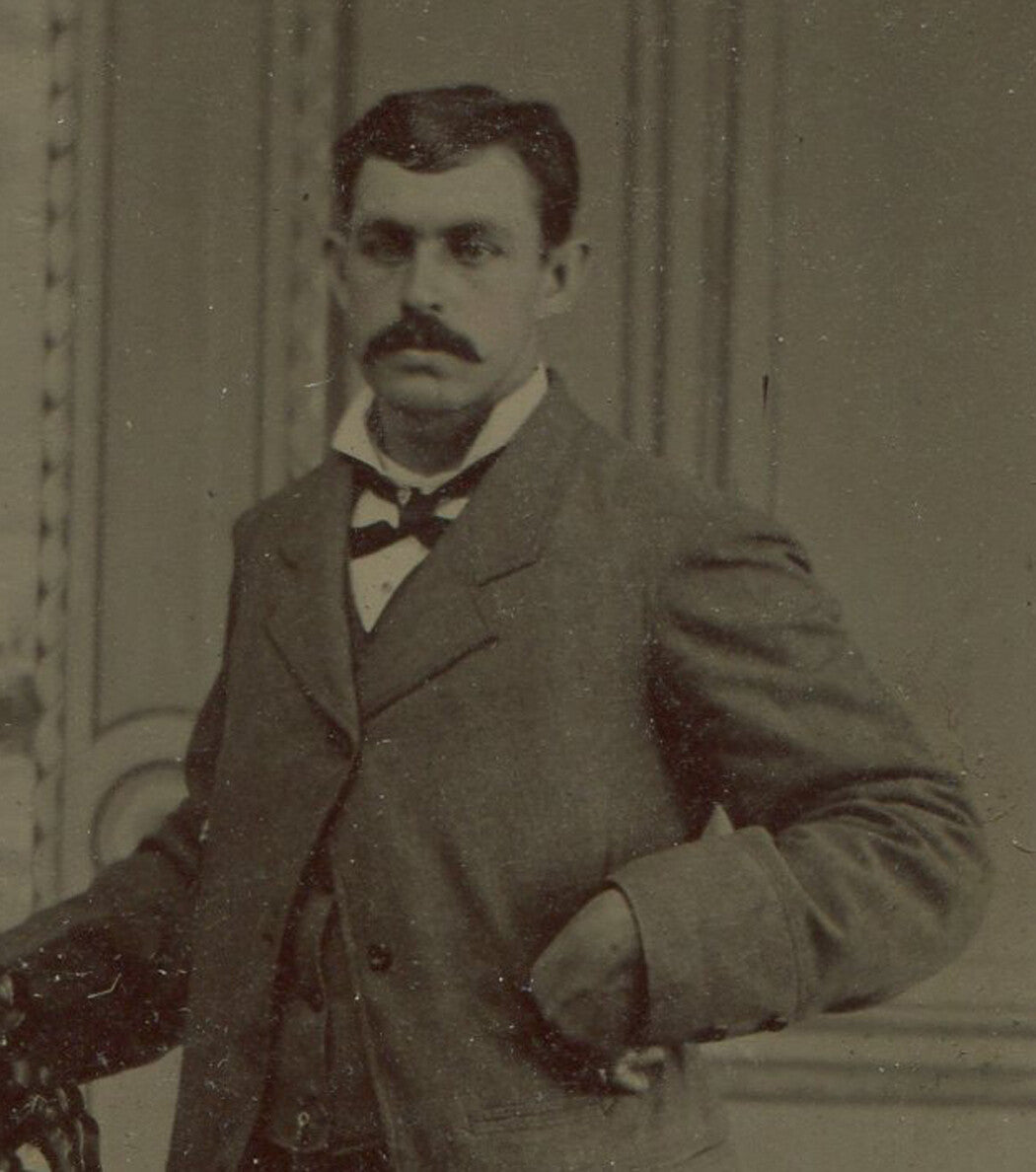 MAN POSED STANDING AT CHAIR, HAND IN COAT POCKET. TINTYPE.