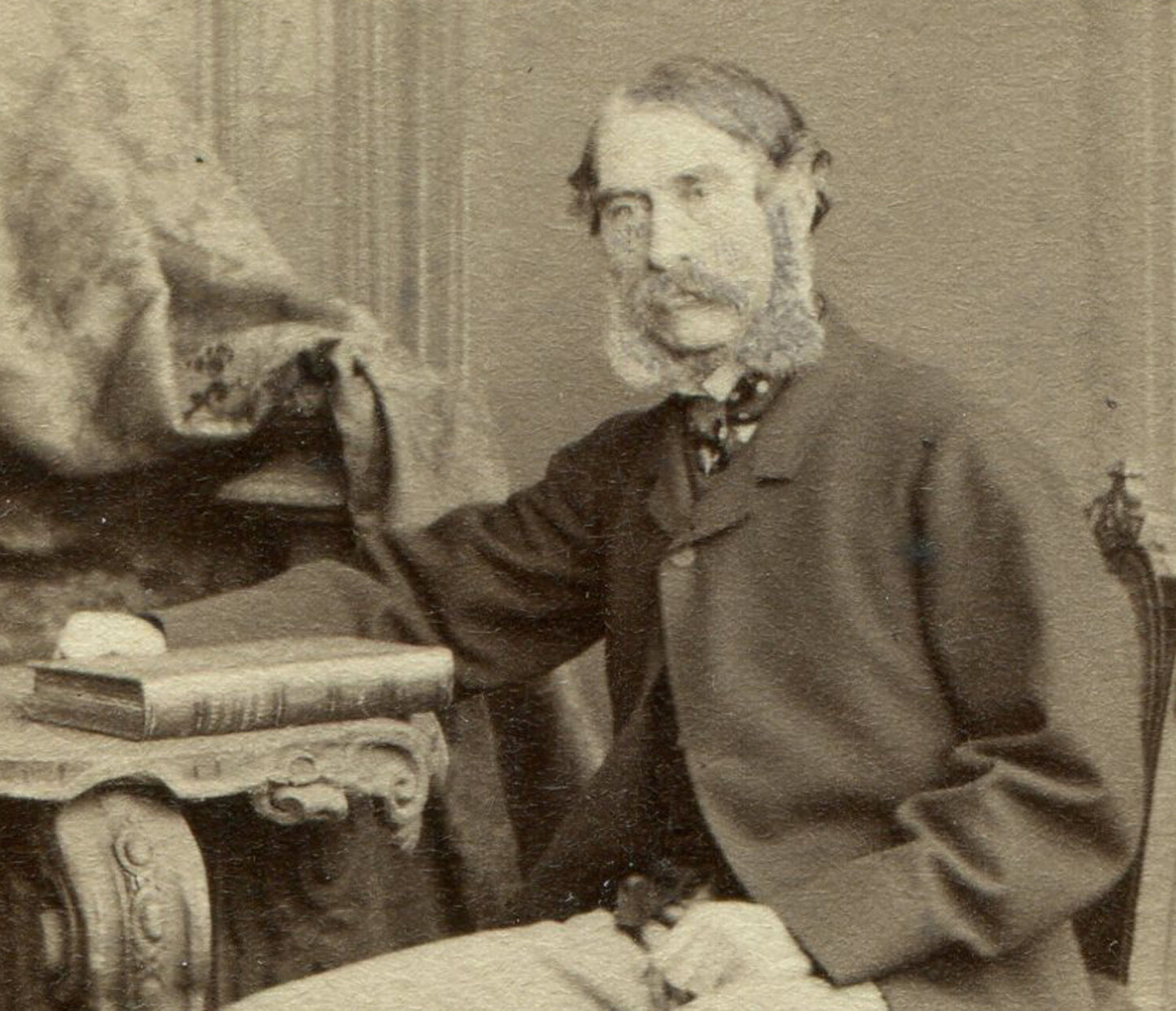MAN W/THICK MUTTON CHOPS SEATED AT TABLE W/BOOKS. I.D. COL LANGLEY OF LONDON.