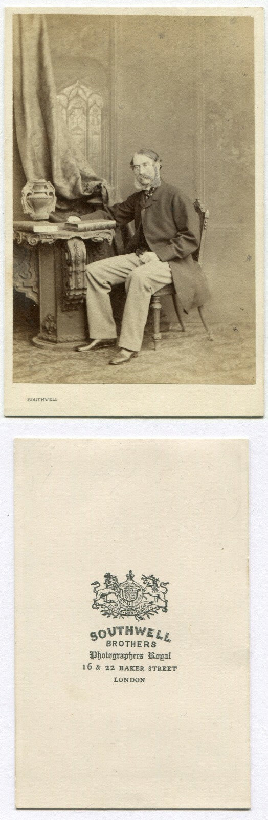 MAN W/THICK MUTTON CHOPS SEATED AT TABLE W/BOOKS. I.D. COL LANGLEY OF LONDON.