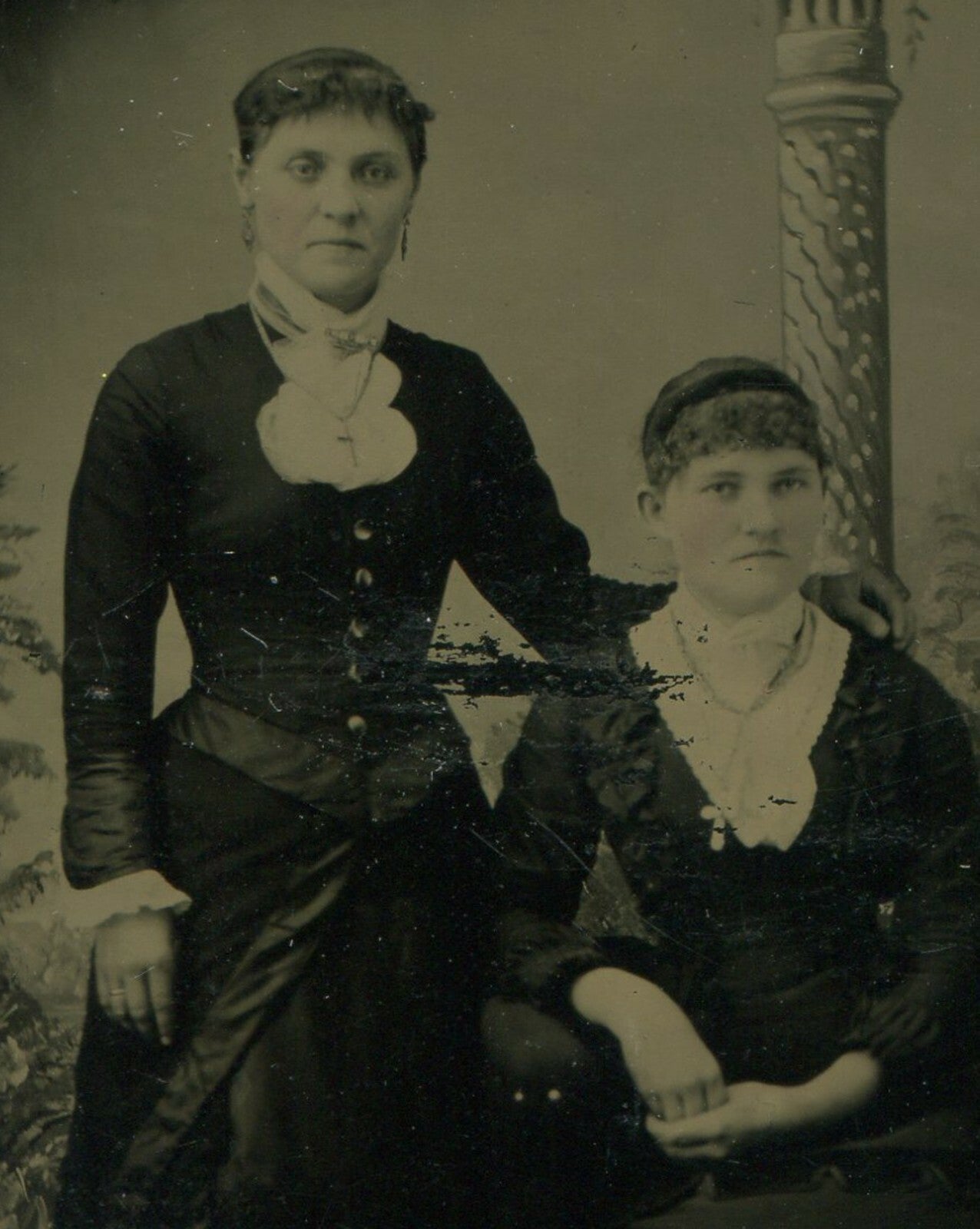 Vintage tintype portrait: two women, painted background, unhappy expressions,