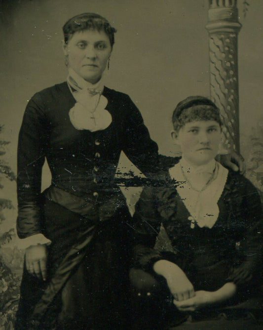 Vintage tintype portrait: two women, painted background, unhappy expressions,