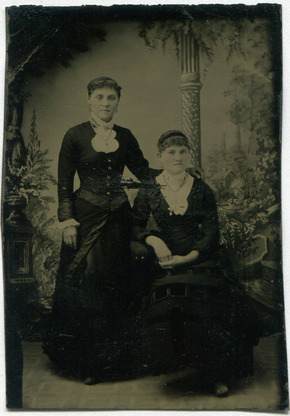 Vintage tintype portrait: two women, painted background, unhappy expressions,