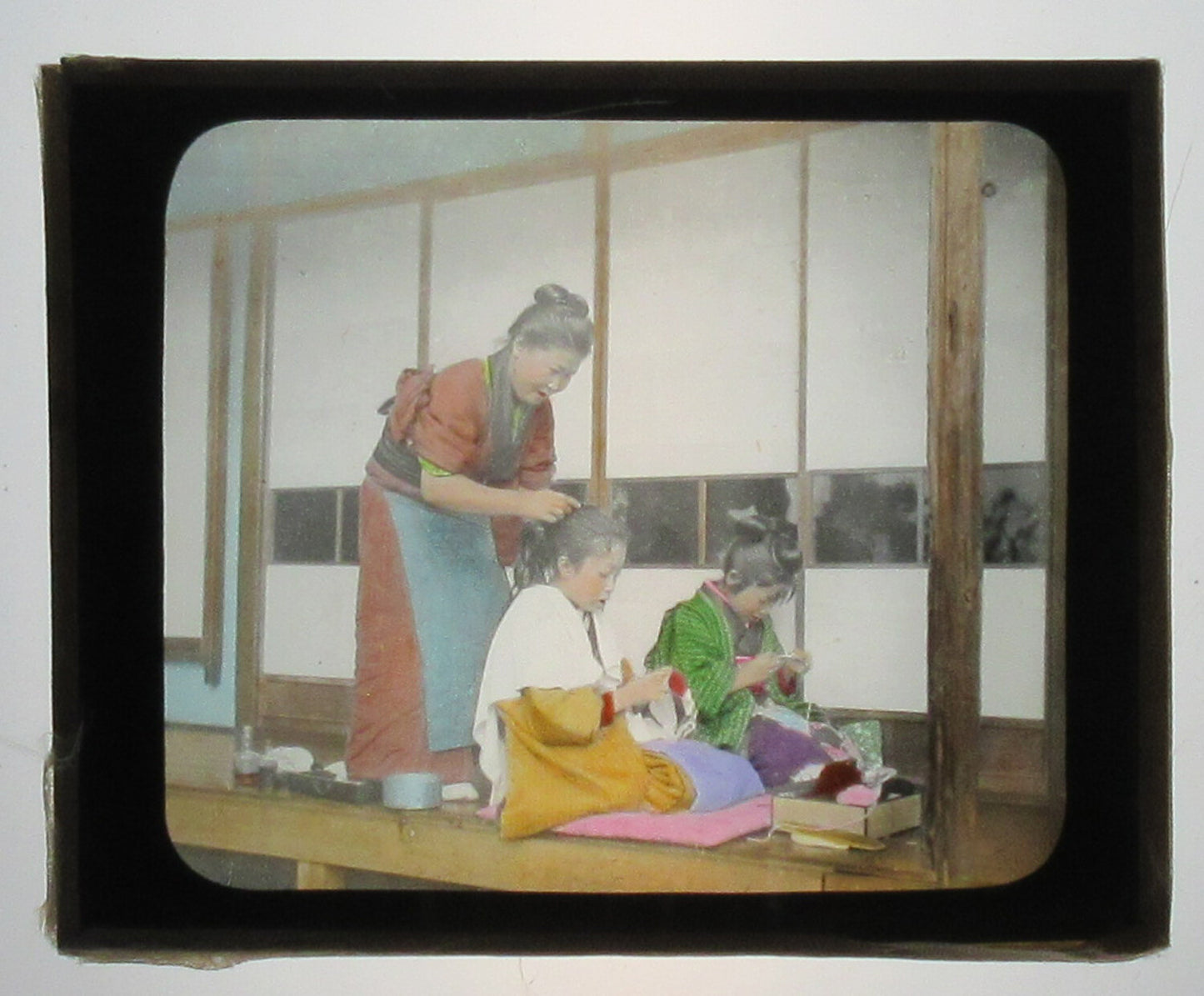 JAPANESE MOTHER TENDING TO DAUGHTERS HAIR. HAND COLORED PHOTO ON GLASS.