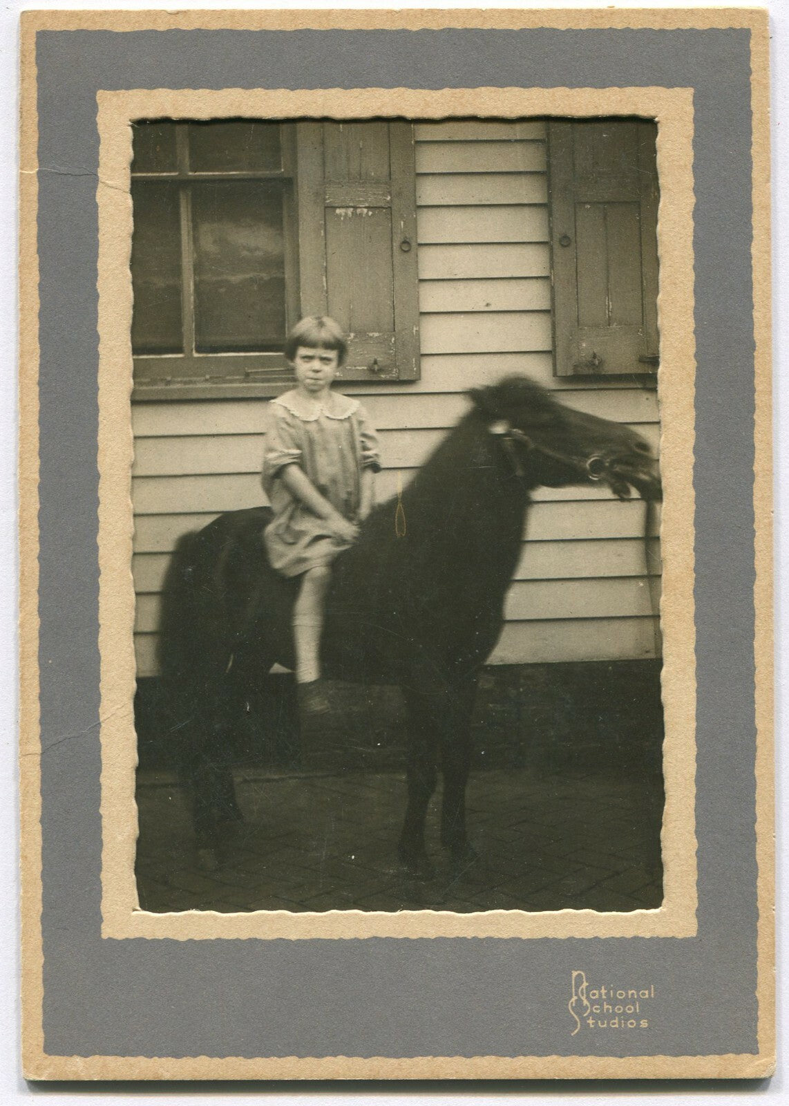 GRUMPY LITTLE GIRL ON A PONY. 6X4.25 B&W IN NATIONAL SCHOOL STUDIOS PAPER FRAME