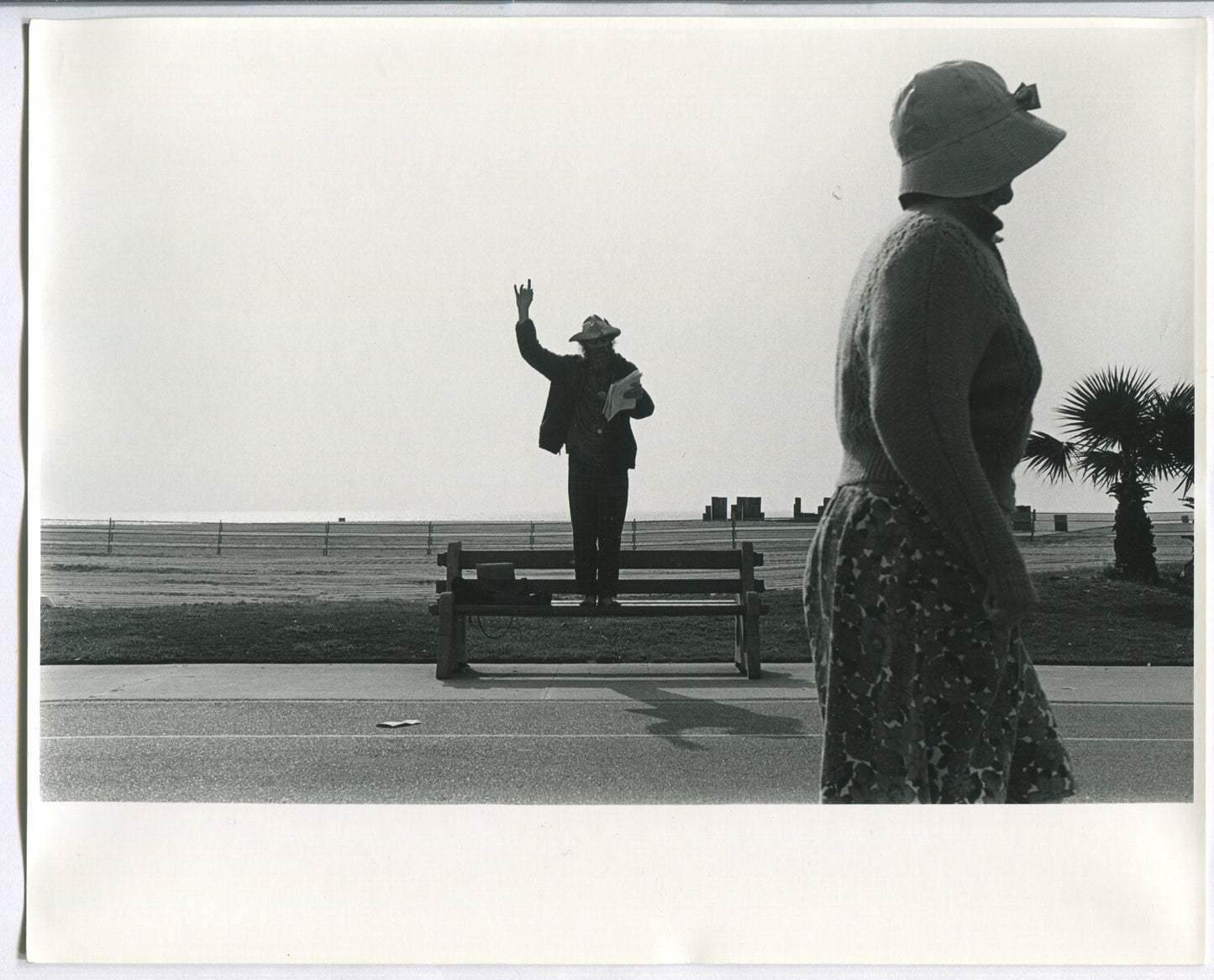 MAN SPEAKING WHILE STANDING ON PARK BENCH. B&W 8X10.1970s.