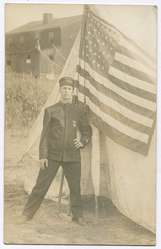 Vintage Photo Postcard: Firefighter in Uniform with Flag (1900s) – Historic Fire