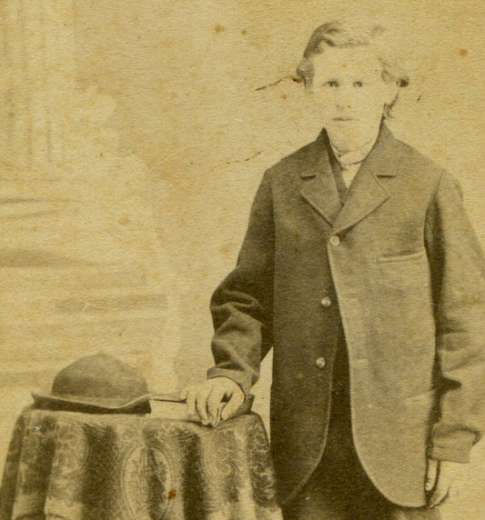 TALL GAUNT BOY IN BAGGY SUIT, HAT ON TABLE. CDV.