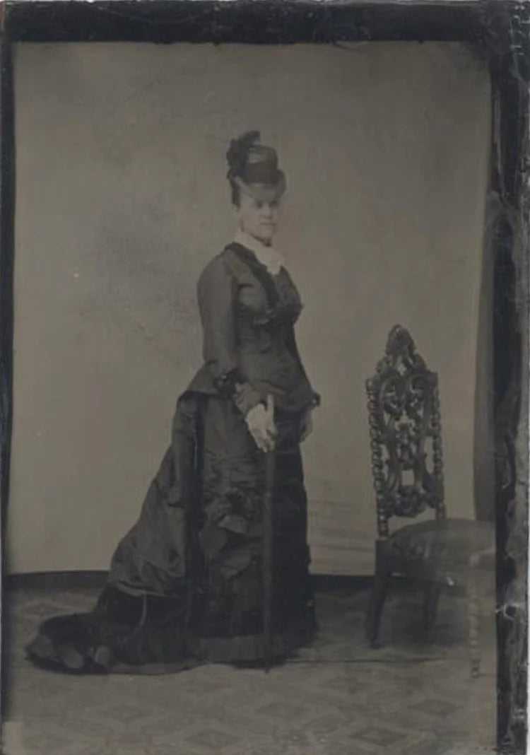 TINTYPE, WOMAN STANDING WITH CHAIR WEARING A FANCY DRESS AND FEATHERED HAT.