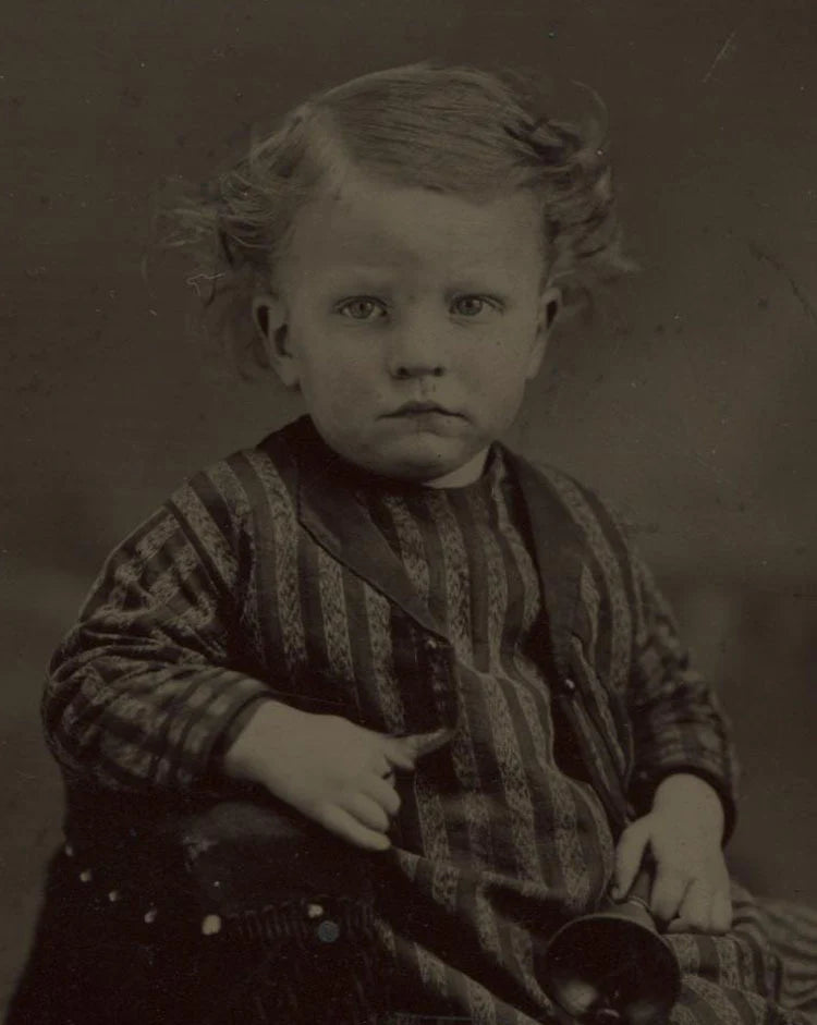 TINTYPE YOUNG CHILD IN STRIPED AND CHECK OUTFIT HOLDING A BELL. TINTED. UNHAPPY.